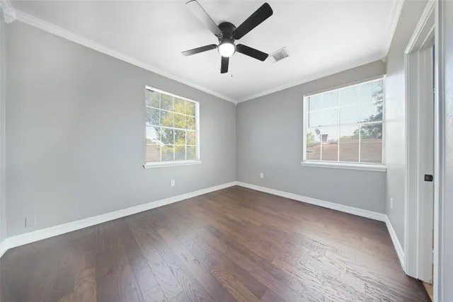 an empty room with wooden floor ceiling fan and windows