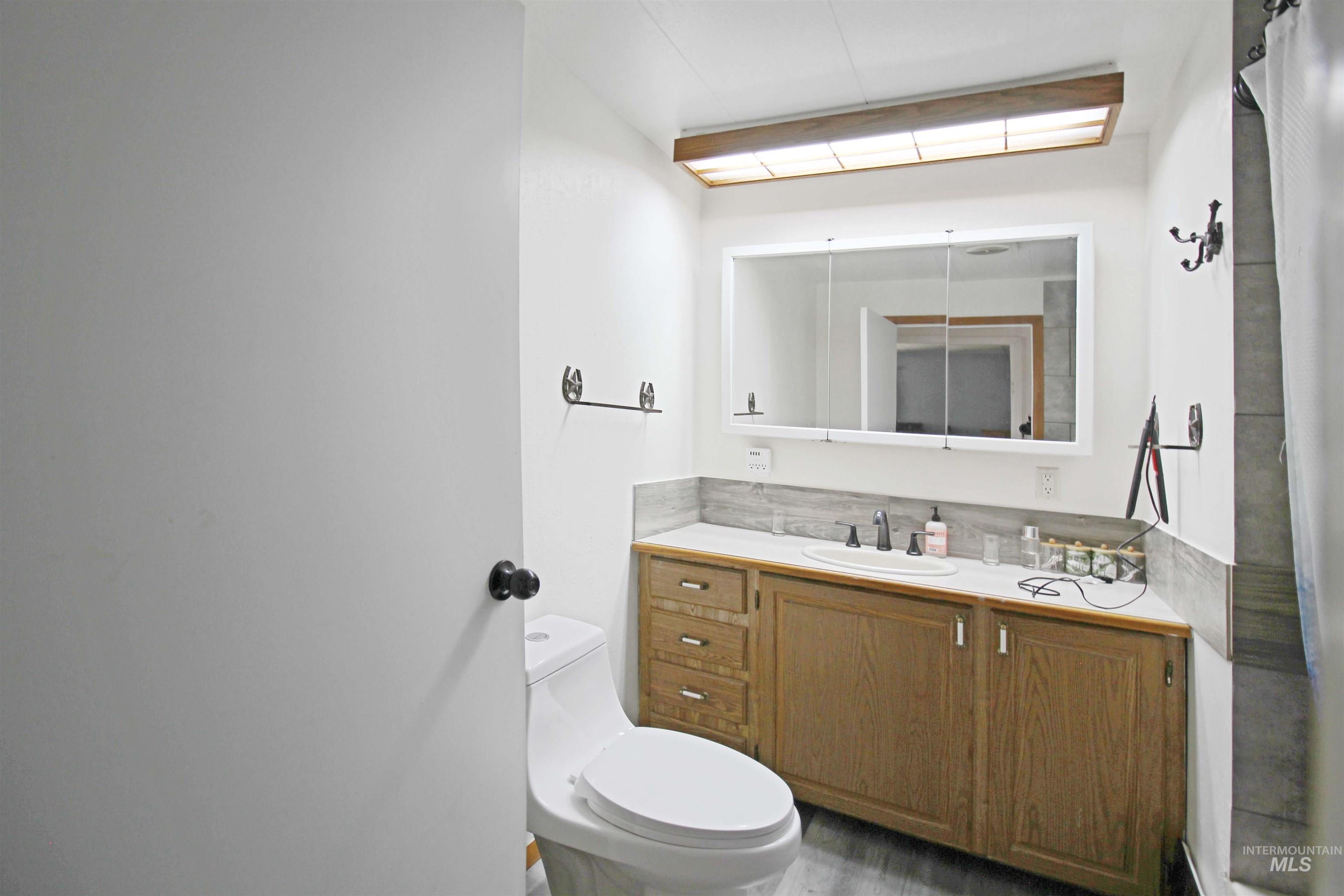 1265 Pioneer Road Weiser, ID 83672 - Photo 20 of 29 Bathroom featuring a wood-finish vanity with an integrated sink, a large mirrored medicine cabinet, and a coordinating stone-finish backsplash