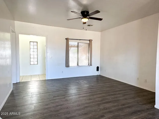 an empty room with wooden floor chandelier fan and windows