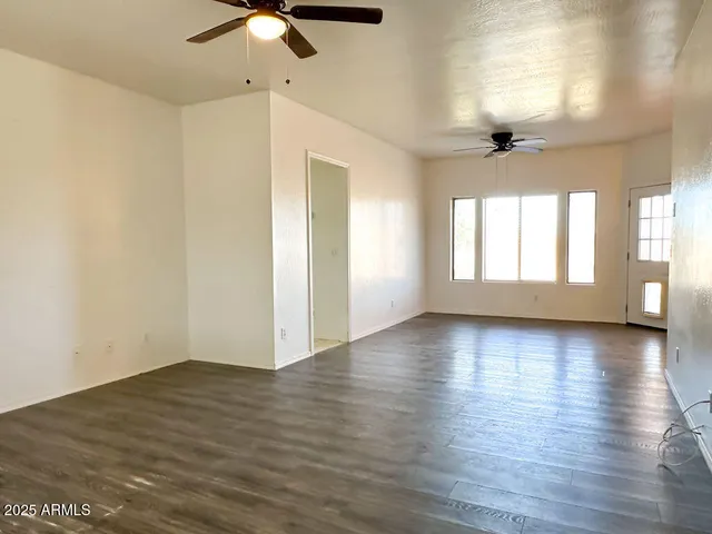 an empty room with wooden floor chandelier fan and windows