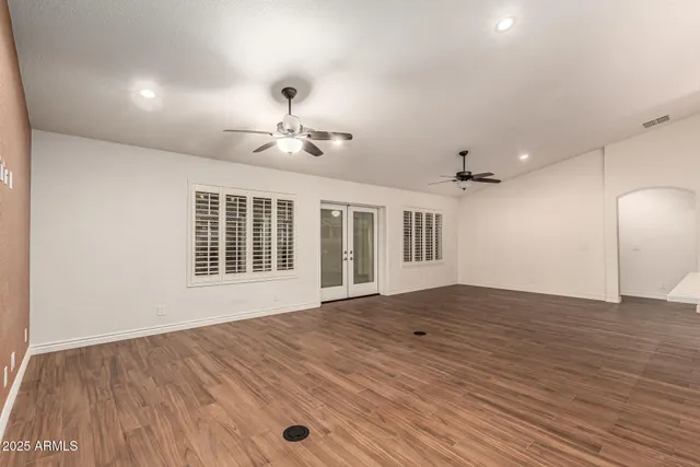 an empty room with wooden floor ceiling fan and windows