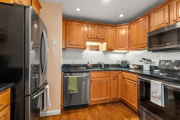 a kitchen with stainless steel appliances granite countertop a stove top oven a refrigerator and a sink with wooden floor