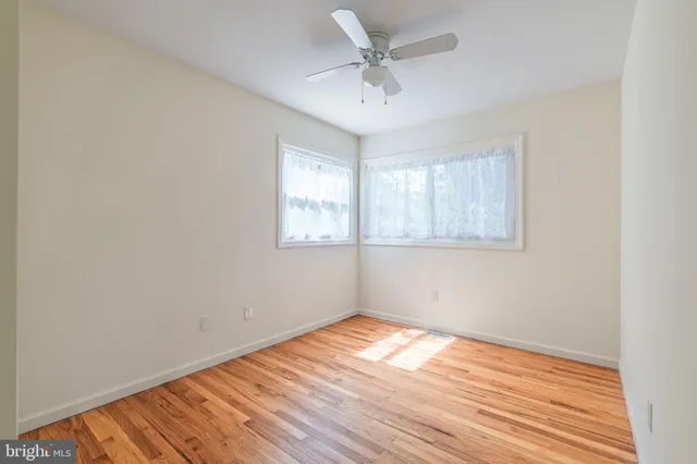 an empty room with wooden floor fan and windows
