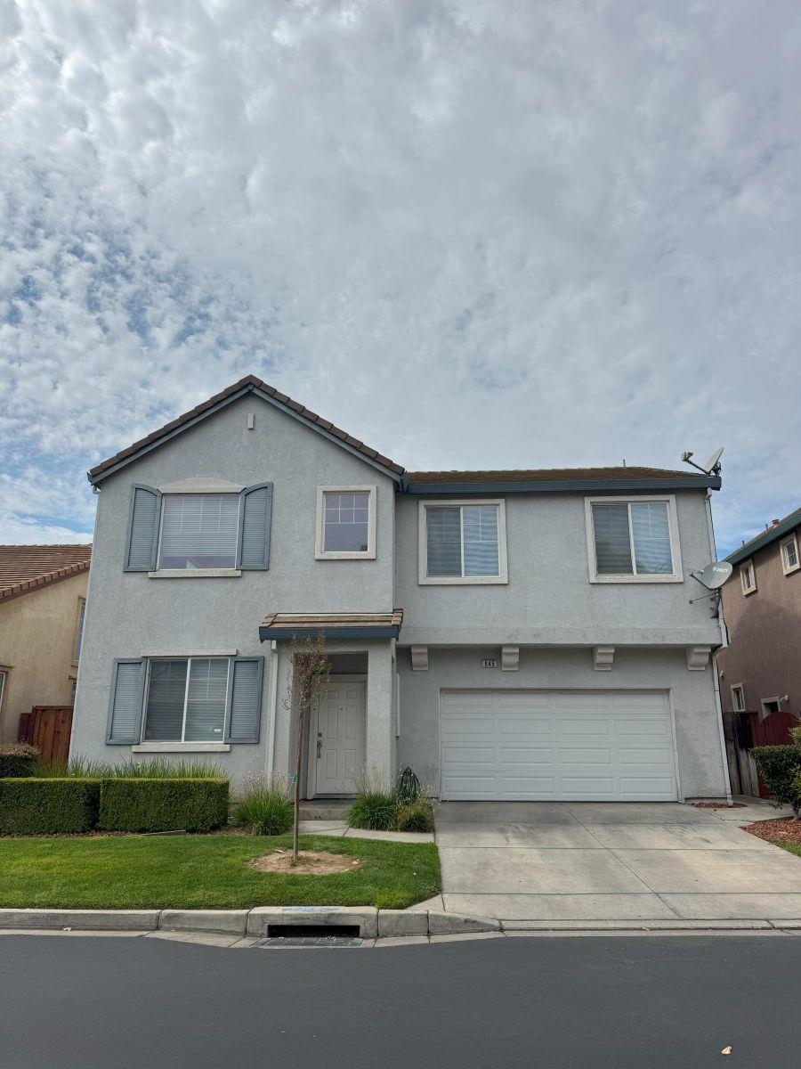 Traditional home featuring concrete driveway, stucco siding, a garage, and a front yard
