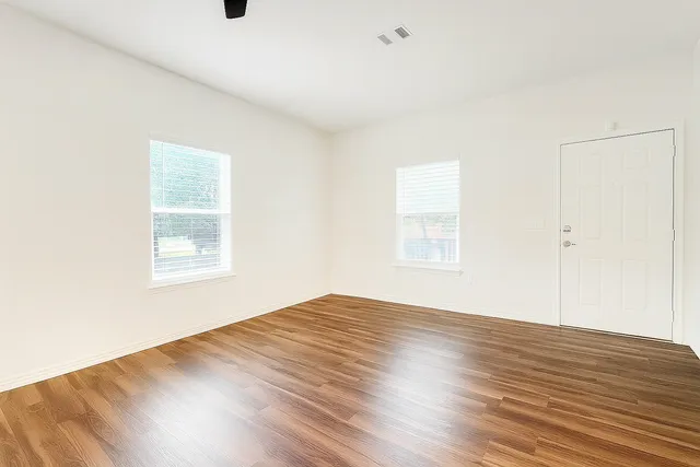 a view of an empty room with wooden floor and a window