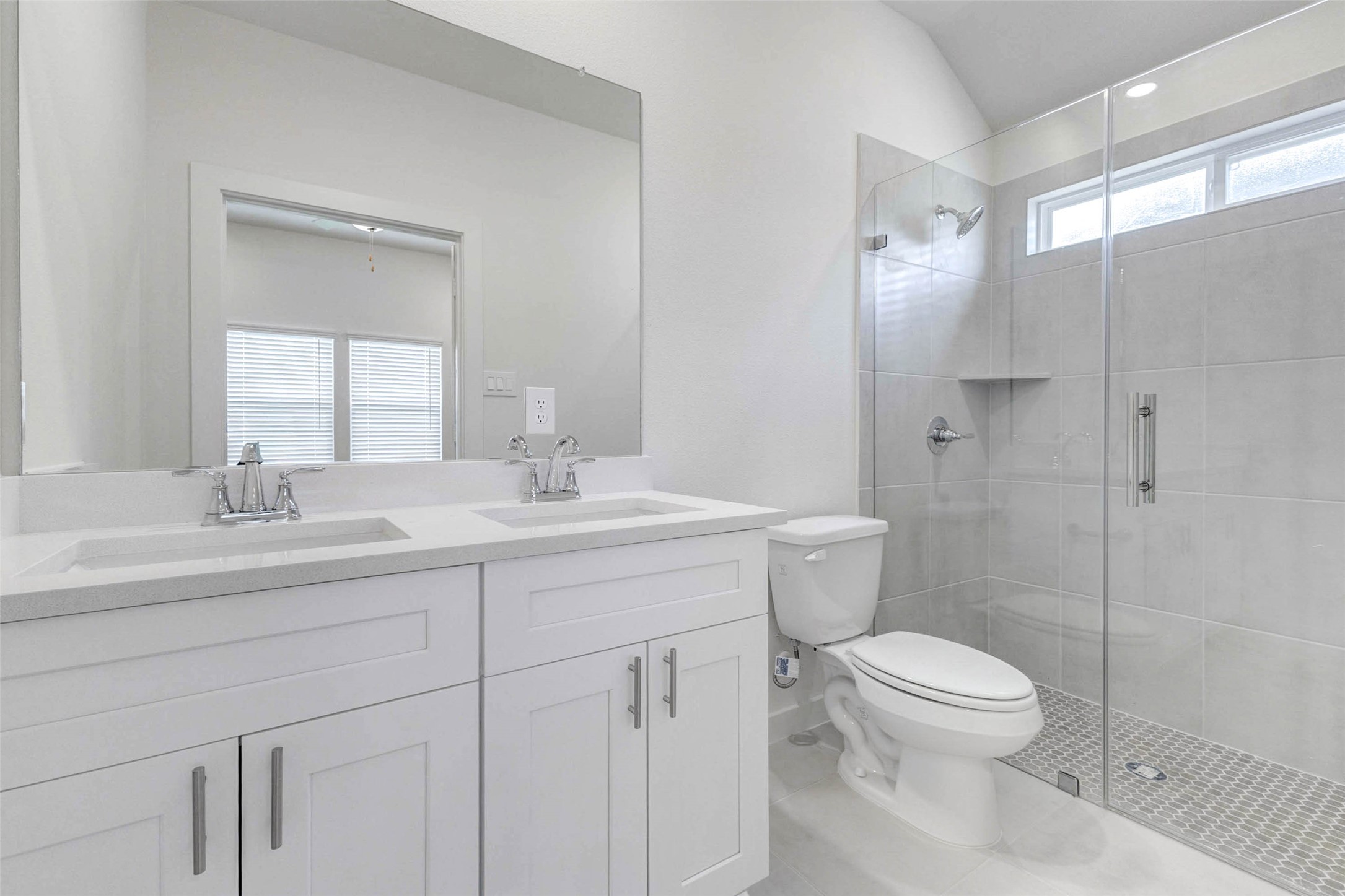 6475 Escondido Drive Rosharon, TX 77583 - Photo 19 of 32 The bathroom features a bright double vanity with white cabinetry, sleek countertops, chrome fixtures, and a large mirror. A glass-enclosed shower with neutral tile, built-in niche, and modern finishes adds a clean, spa-like feel, making this space both stylish and practical.