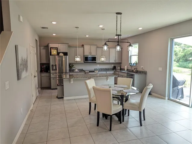 a dining area with stainless steel appliances kitchen island granite countertop a dining table chairs and a refrigerator