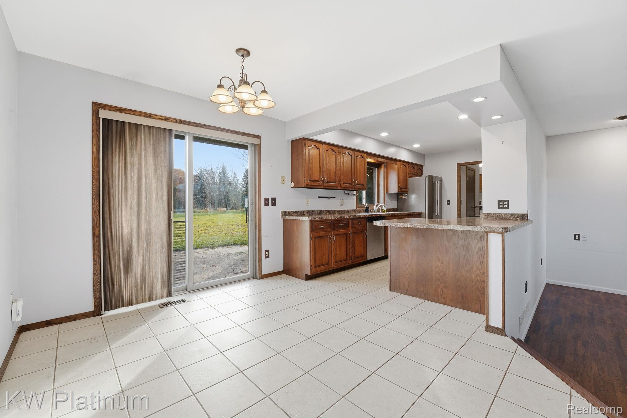 7383 Fisher Road Jeddo, MI 48032 - Photo 6 of 40 Kitchen featuring brown cabinets, light tile patterned floors, a peninsula, decorative light fixtures, and a chandelier