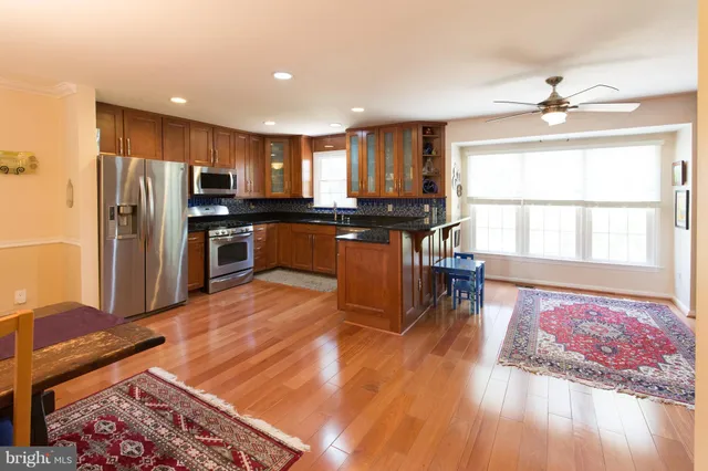 a kitchen with stainless steel appliances granite countertop a refrigerator a stove top oven and a dining table with wooden floor