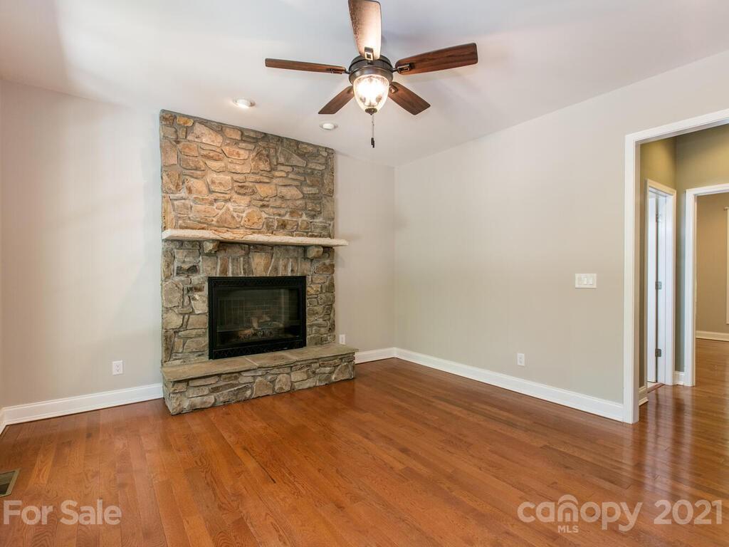 356 Green Hills Road Mill Spring, NC 28756 - Photo 13 of 31 an empty room with windows a fireplace a ceiling fan and wooden floor