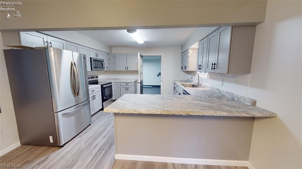 1715 Chenango Road Wakeman, OH 44889 - Photo 7 of 21 Kitchen with sink, appliances with stainless steel finishes, light stone counters, light wood-type flooring, and kitchen peninsula