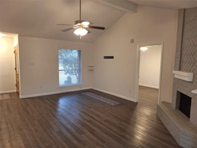 an empty room with wooden floor fireplace and windows
