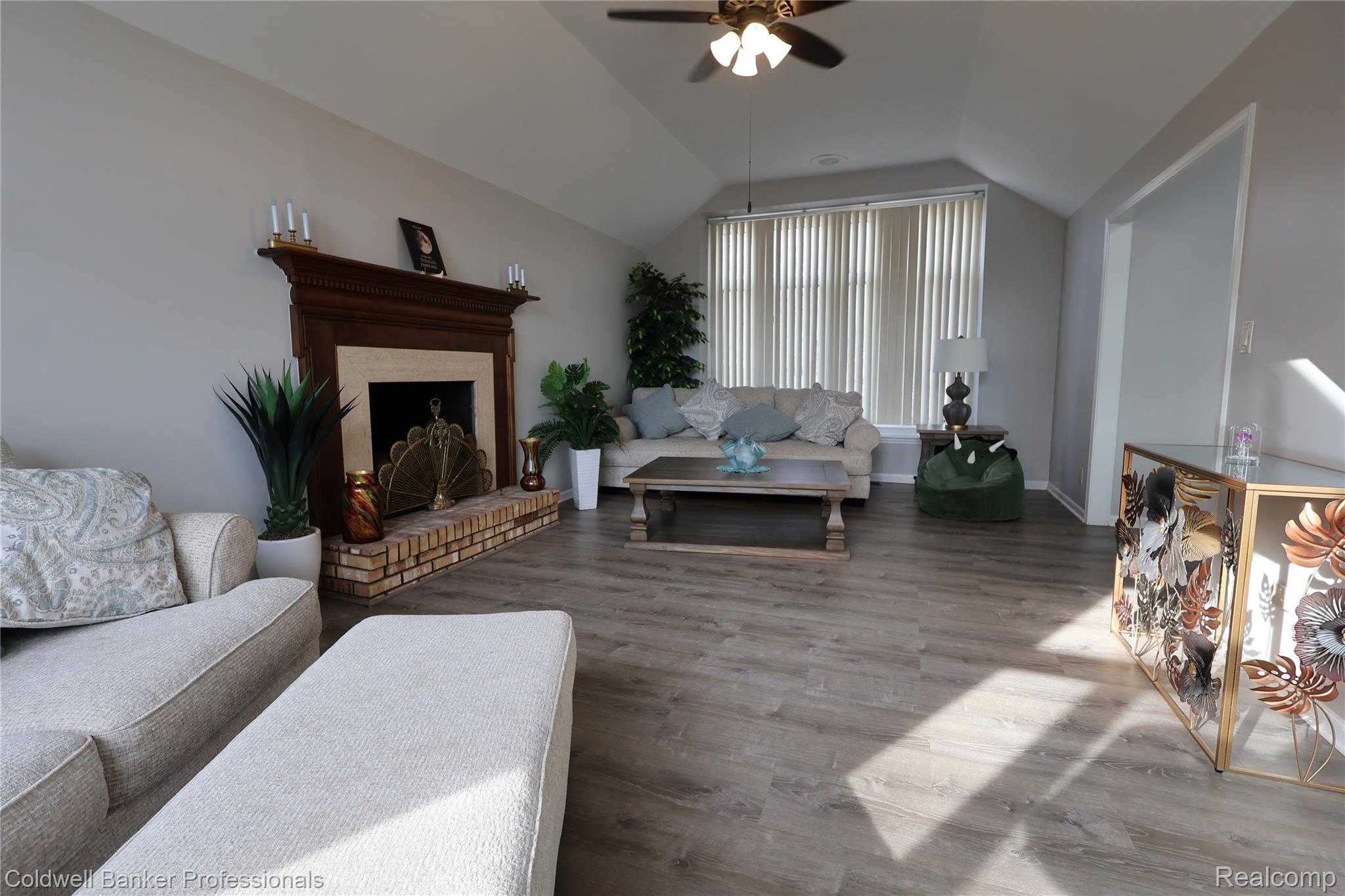 Living area with wood finished floors, a brick fireplace, a ceiling fan, and lofted ceiling