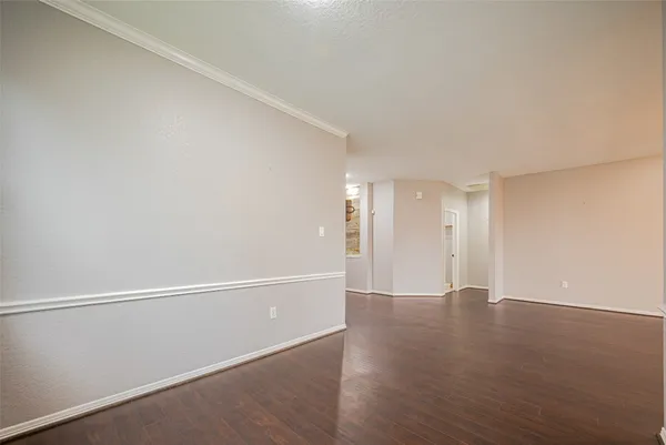 a view of an empty room with wooden floor and a kitchen