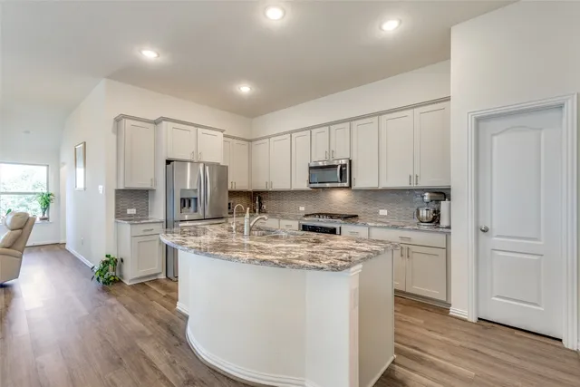 a kitchen with stainless steel appliances granite countertop a stove a sink dishwasher a refrigerator and white cabinets with wooden floor