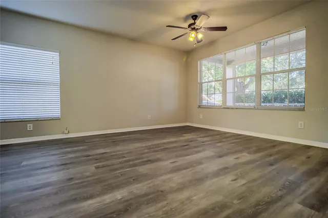 an empty room with wooden floor fan and windows