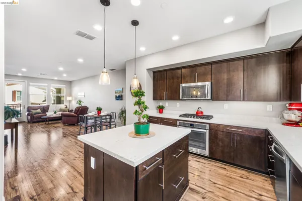 a kitchen with a stove a refrigerator a sink dishwasher with wooden cabinets and couches