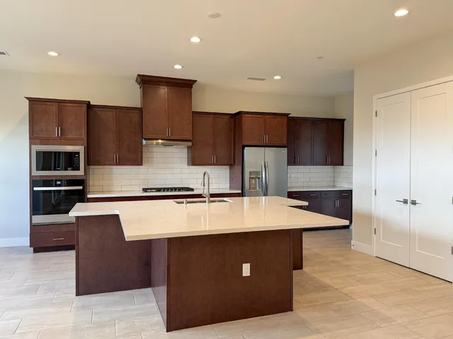 a large kitchen with stainless steel appliances kitchen island granite countertop a stove a refrigerator and a sink with wooden cabinets