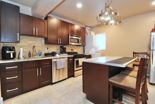 a kitchen with stainless steel appliances granite countertop wooden cabinets a sink dishwasher a stove and a refrigerator with wooden floor