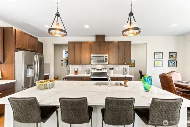 a kitchen with stainless steel appliances kitchen island granite countertop a dining table chairs and a refrigerator