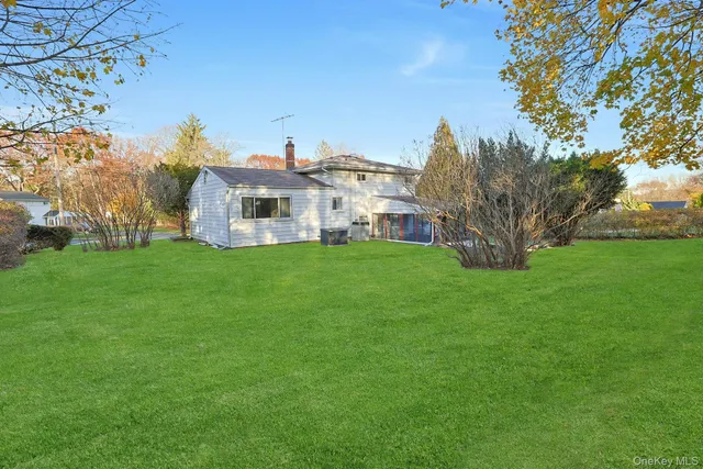 a house that is sitting in the grass with large trees and plants