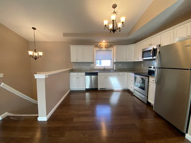 a kitchen with stainless steel appliances granite countertop a refrigerator a sink dishwasher a stove and white cabinets with wooden floor