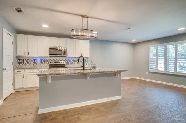 a kitchen with kitchen island granite countertop stainless steel appliances a sink a stove a refrigerator cabinets and a window