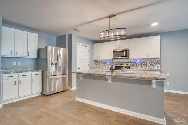 a kitchen with stainless steel appliances granite countertop a refrigerator a stove a sink dishwasher a refrigerator and white cabinets with wooden floor