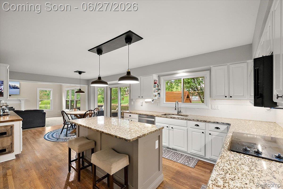 4193 Oak Tree Circle Rochester, MI 48306 - Photo 16 of 72 Open-concept kitchen featuring an island with pendant lighting, stone countertops, white cabinetry, and wood flooring