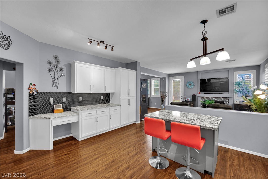 1724 Millstream Way Henderson, NV 89074 - Photo 13 of 60 An open-concept living space seamlessly connects the kitchen and living room, featuring rich hardwood flooring and sleek white cabinetry.