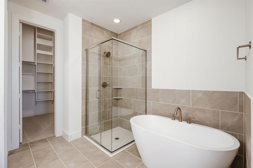 4314 Haley Way Oak Point, TX 75068 - Photo 21 of 28 Contemporary bathroom featuring a freestanding soaking tub, glass-enclosed shower, neutral tile surround, recessed lighting, and a walk-in closet with built-in shelving
