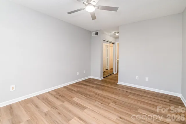 an empty room with wooden floor chandelier fan and windows