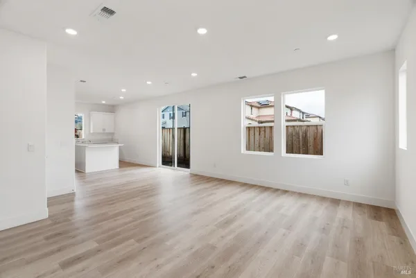 a view of an empty room with wooden floor and a kitchen