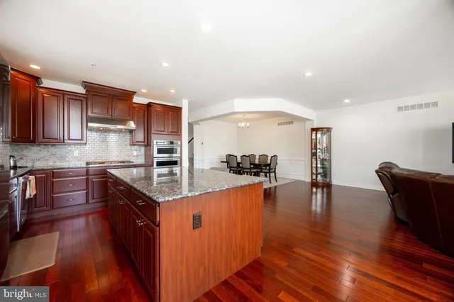 a kitchen with stainless steel appliances granite countertop a stove top oven a sink a dining table and chairs with wooden floor