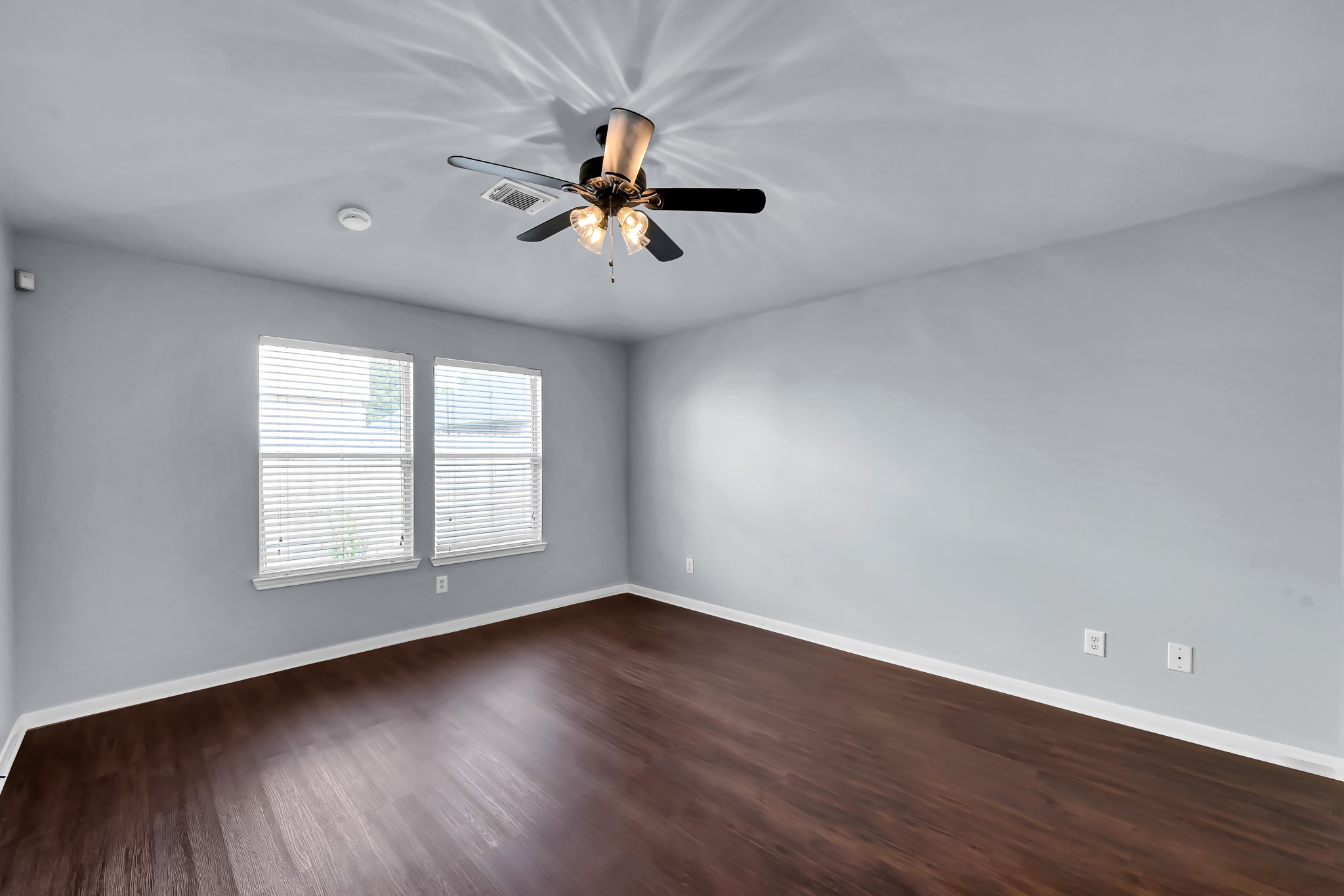7811 Holly Berry Court Cypress, TX 77433 - Photo 11 of 24 This room features a sleek, modern design with dark wood flooring, light gray walls, and ample natural light from two large windows. A ceiling fan with lights adds functionality and style.