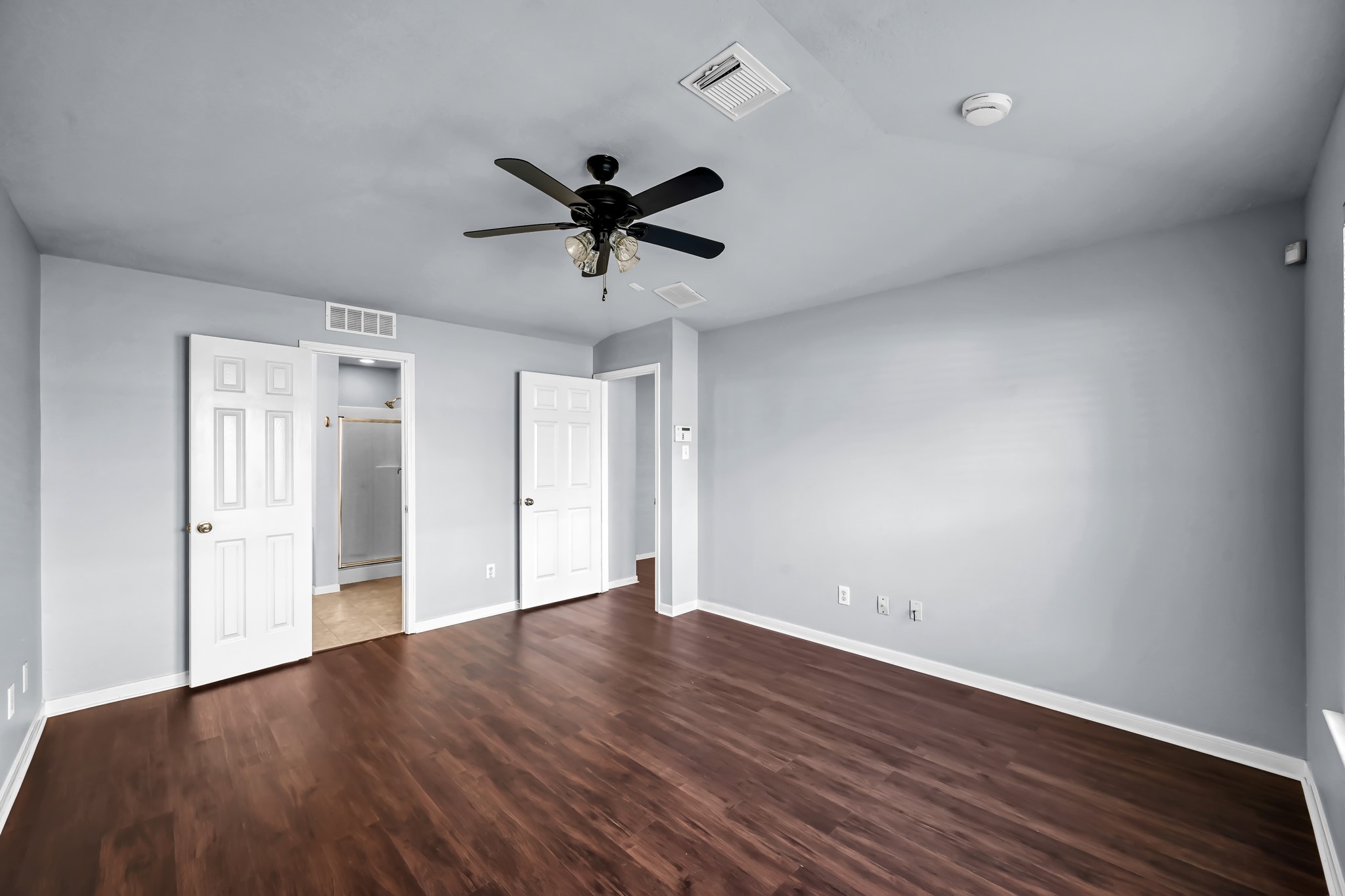 7811 Holly Berry Court Cypress, TX 77433 - Photo 12 of 24 This room features fresh gray walls, darklaminated flooring, and a ceiling fan. It includes two doors leading to a walk-in closet and an adjoining bathroom, offering convenience and ample storage.