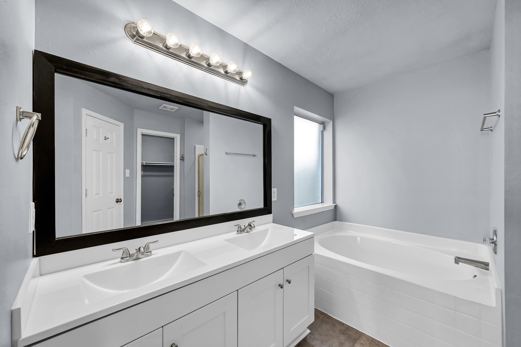 7811 Holly Berry Court Cypress, TX 77433 - Photo 14 of 24 This bathroom features a modern double vanity with a large framed mirror, ample lighting, and a spacious soaking tub. The neutral color palette and frosted window provide a bright, relaxing atmosphere.