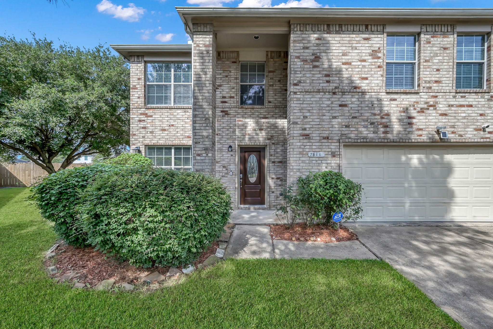 7811 Holly Berry Court Cypress, TX 77433 - Photo 2 of 24 This photo shows a two-story brick home with a well-maintained front yard. It features a double garage and a welcoming entrance with a glass-paneled door. Large windows provide ample natural light, and there's a lush lawn with neatly trimmed shrubs.