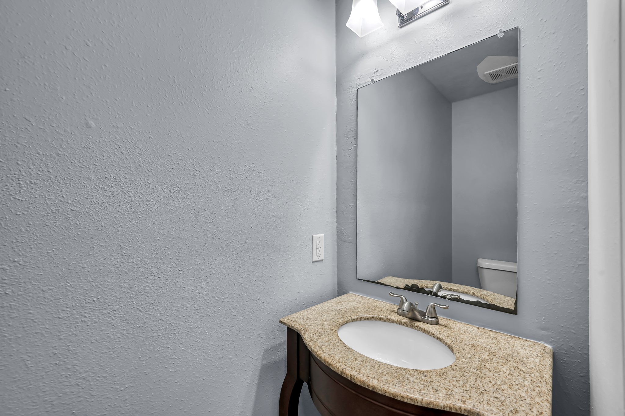 7811 Holly Berry Court Cypress, TX 77433 - Photo 21 of 24 This photo shows a compact bathroom with light gray walls, featuring a granite-topped vanity with an undermount sink. A large mirror is above the sink, and there is a modern light fixture providing illumination.