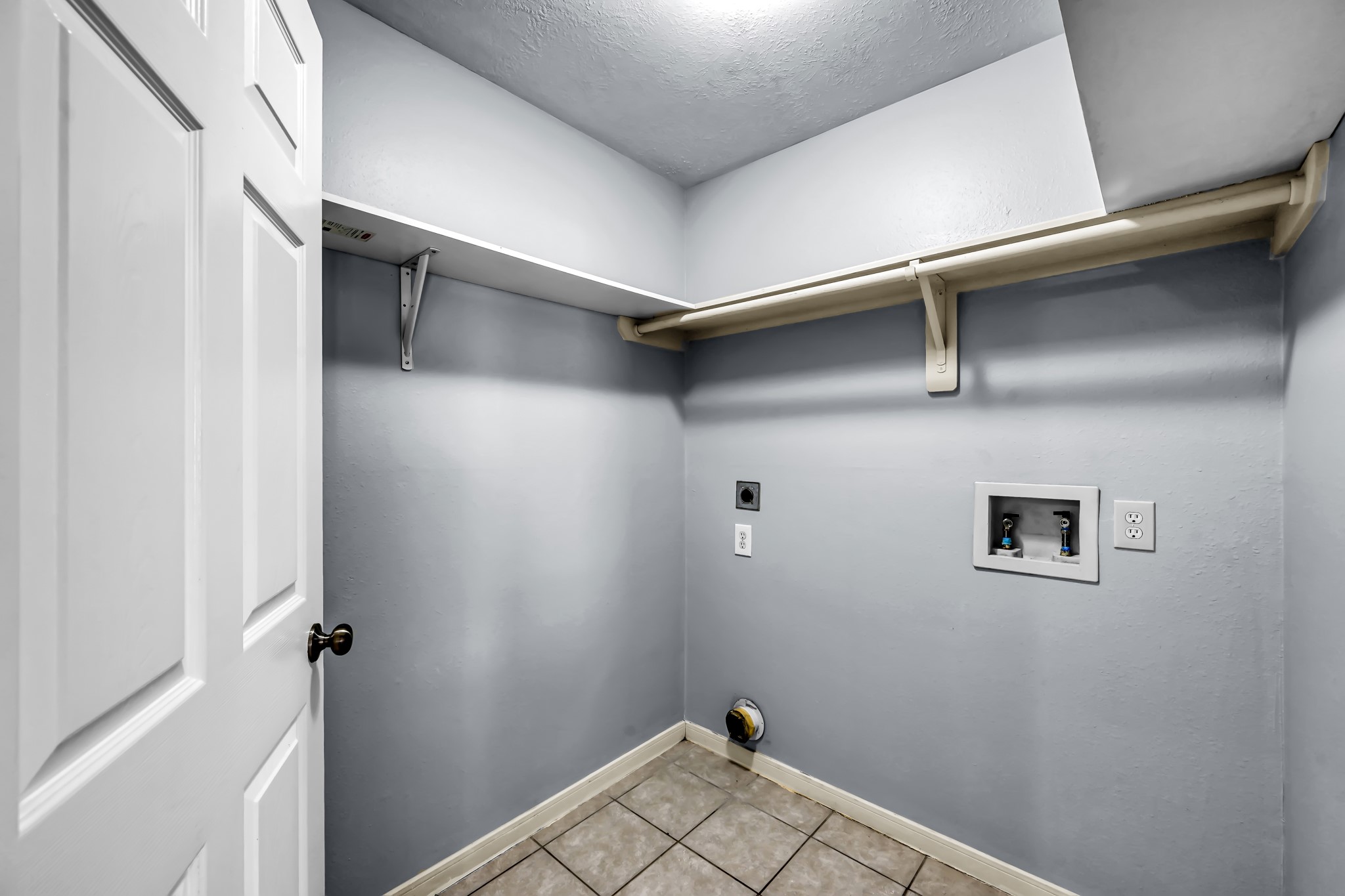 7811 Holly Berry Court Cypress, TX 77433 - Photo 22 of 24 This is a compact laundry room featuring tile flooring, washer and gas dryer hookups, and a shelf for storage. It's functional and ready for appliances.