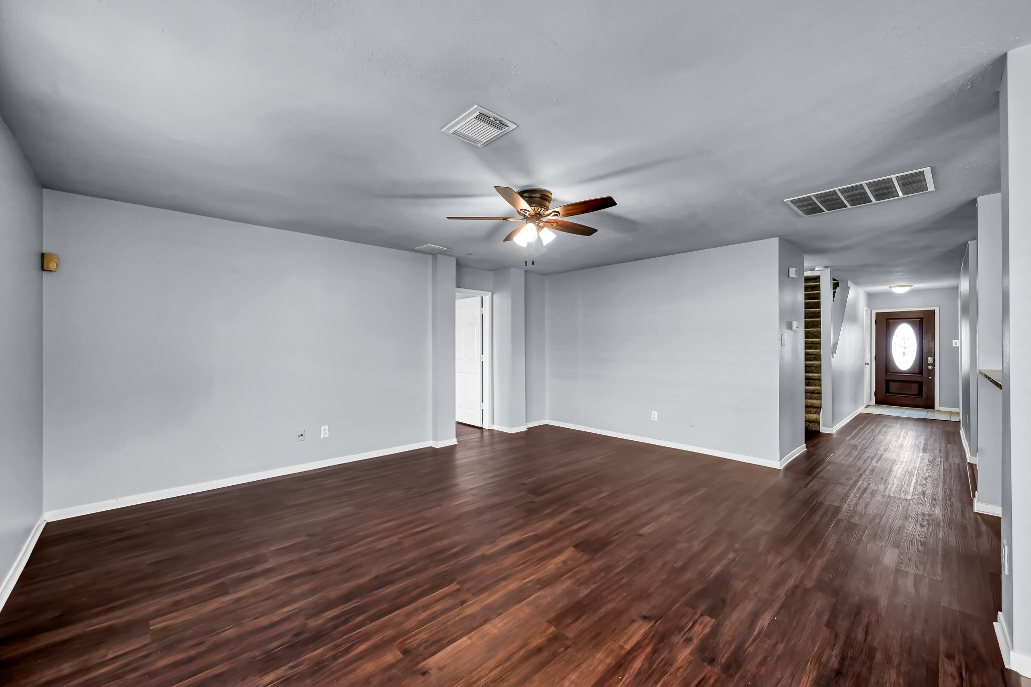 7811 Holly Berry Court Cypress, TX 77433 - Photo 5 of 24 This spacious living area features richlaminated wood flooring, neutral gray walls, and a ceiling fan. It offers an open layout with easy access to adjacent rooms and a view of the front door, creating a welcoming entryway.
