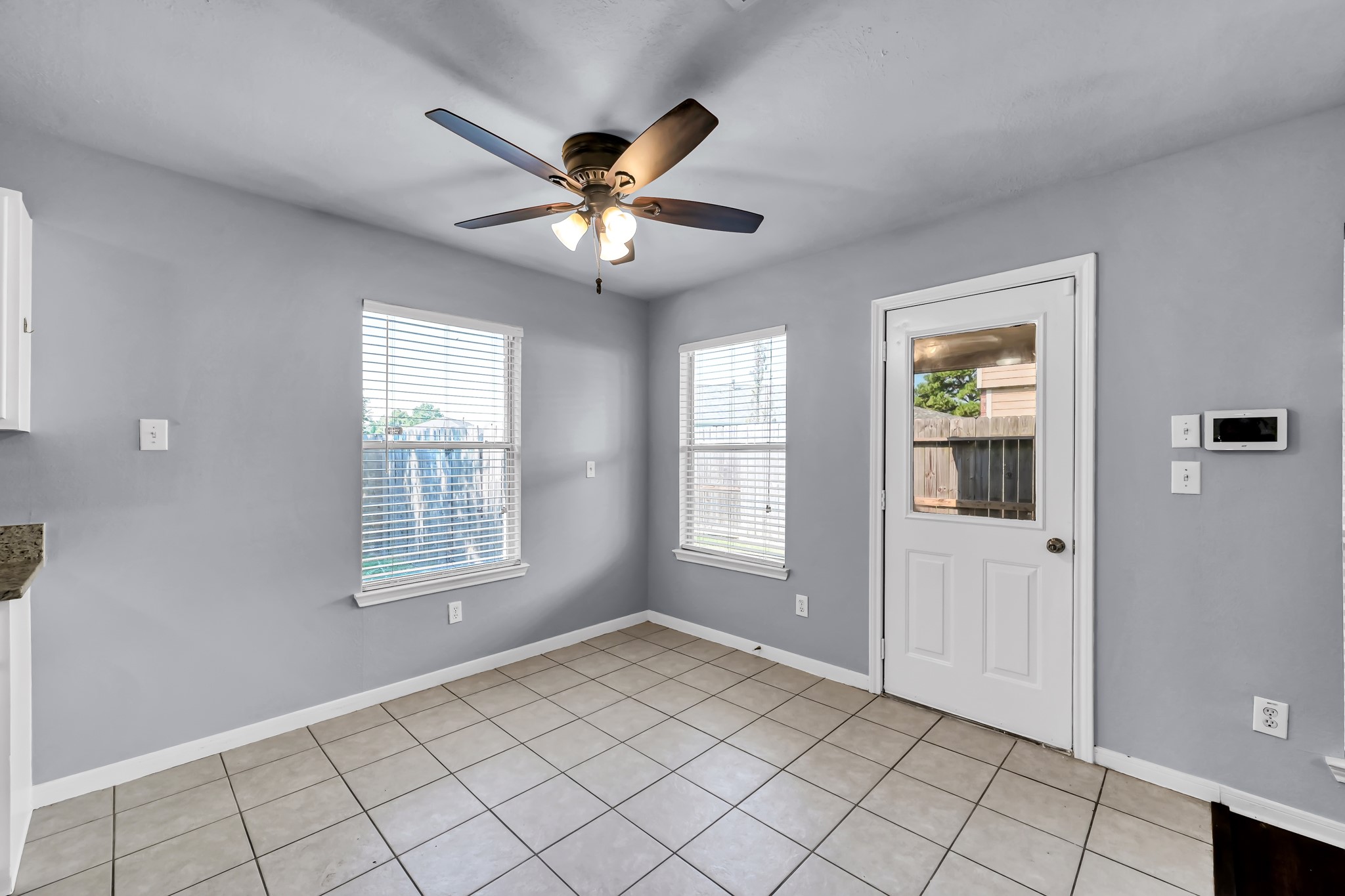 7811 Holly Berry Court Cypress, TX 77433 - Photo 10 of 24 Bright and airy kitchen space with neutral gray walls, tiled flooring, and ample natural light from two windows. Features a ceiling fan and a door leading outside, offering a cozy and functional area.