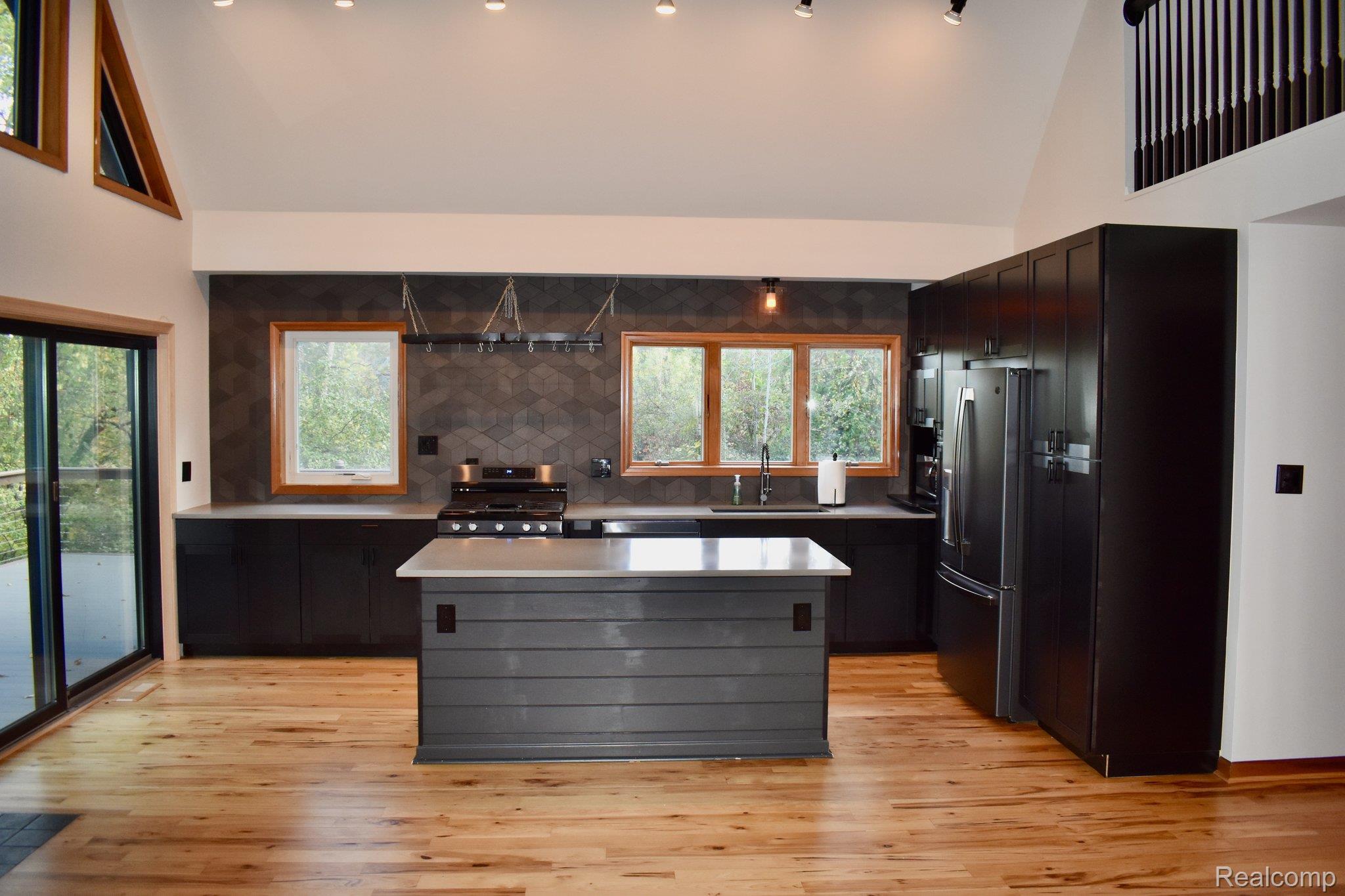 8312 Whitmore Lake Road Brighton, MI 48116 - Photo 26 of 43 Vaulted ceiling, wood-finish flooring, dark cabinetry, hexagon tile backsplash, and a center island with light countertop