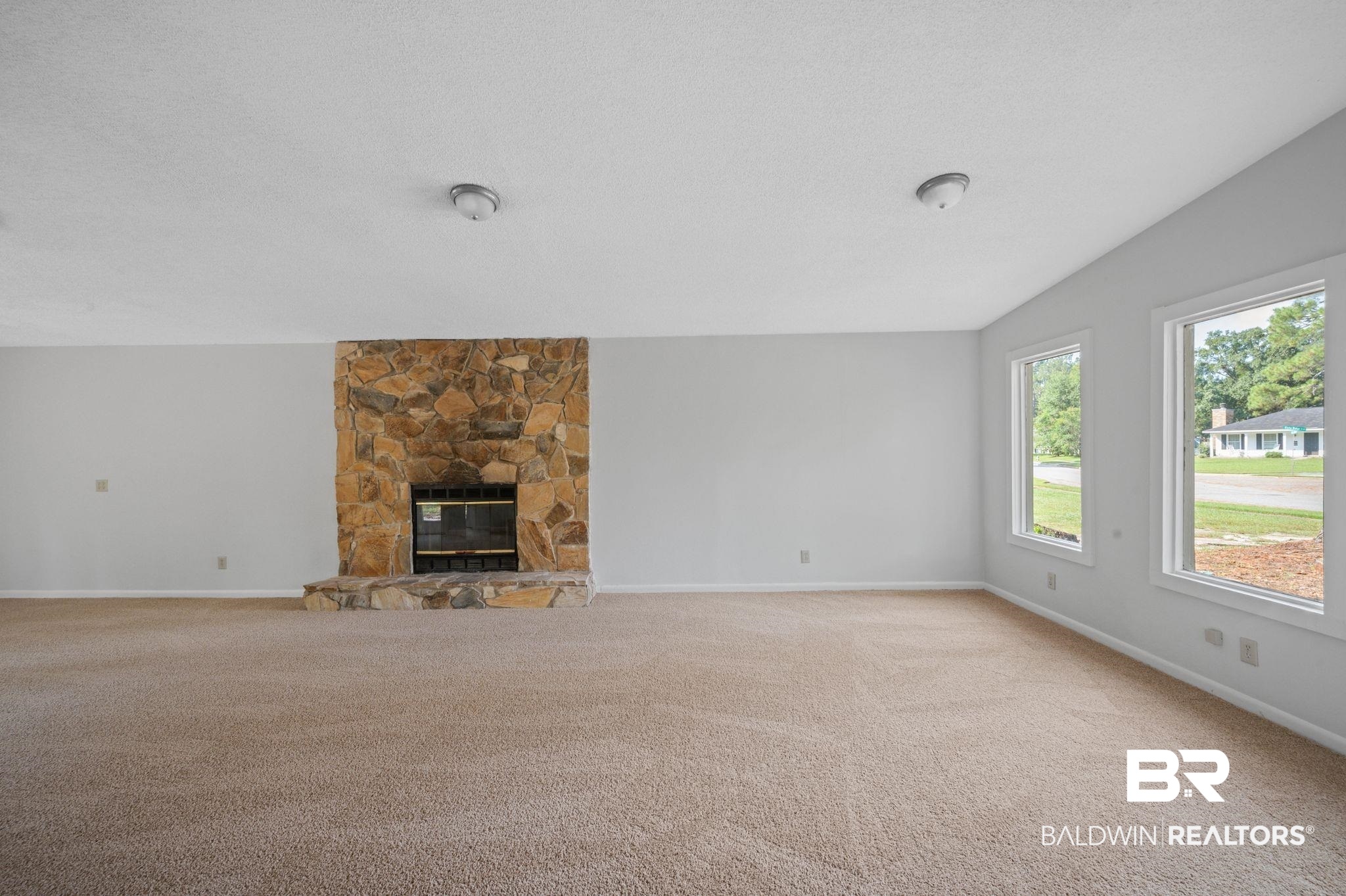 3701 Vista Ridge Drive Mobile, AL 36693 - Photo 18 of 33 Unfurnished living room featuring vaulted ceiling, a stone fireplace, light colored carpet, and a textured ceiling