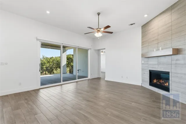 an empty room with wooden floor a ceiling fan a fireplace and windows