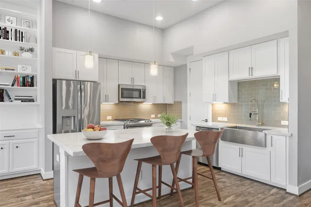 a kitchen with stainless steel appliances a sink a stove a refrigerator cabinets and chairs