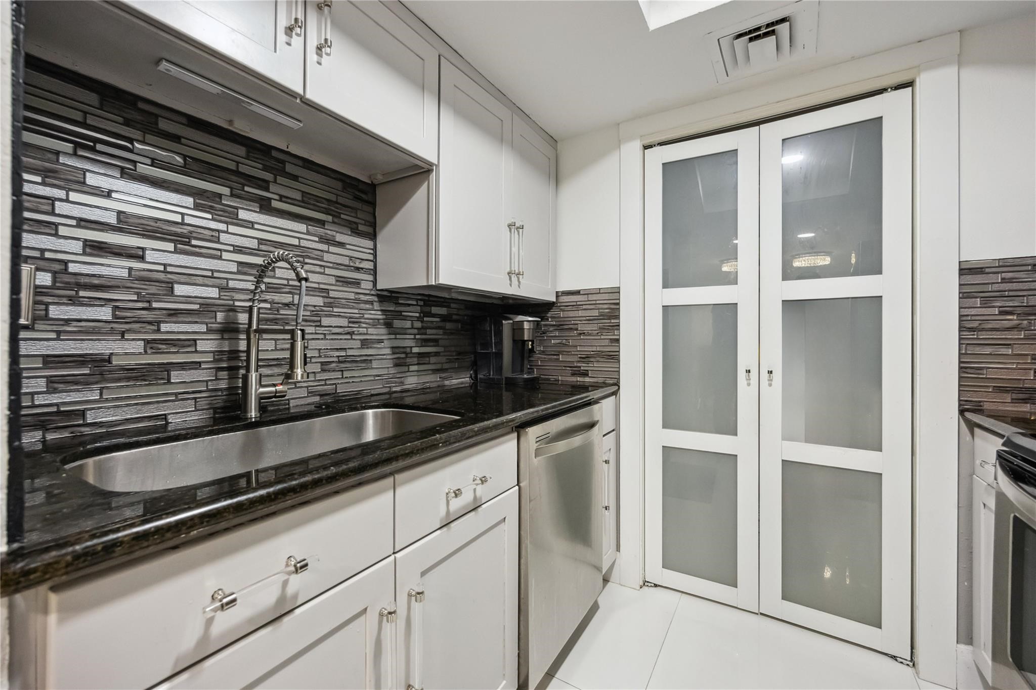 3525 Sage Road, Unit 1713 Houston, TX 77056 - Photo 20 of 25 Sleek kitchen with granite countertops, stainless steel appliances, and a stylish glass-tile backsplash. Hidden behind modern frosted pantry doors, you’ll find a convenient in-unit washer and dryer.