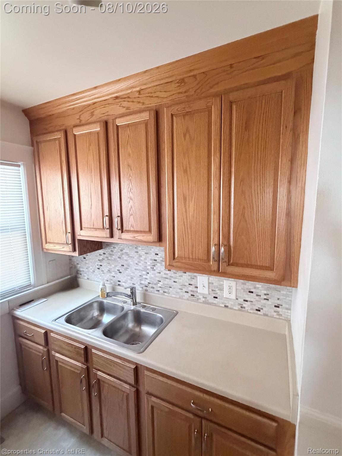 858 Nottingham Road Grosse Pointe, MI 48230 - Photo 9 of 16 Kitchen featuring wood-finish cabinetry, a double basin stainless steel sink, light-toned countertops, and mosaic tile backsplash