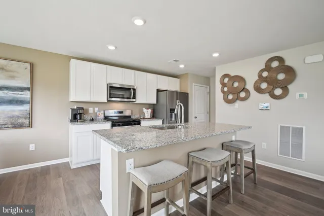 a kitchen with stainless steel appliances granite countertop a refrigerator a stove top oven a sink dishwasher and white cabinets with wooden floor