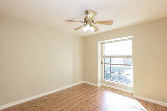 an empty room with wooden floor fan and windows